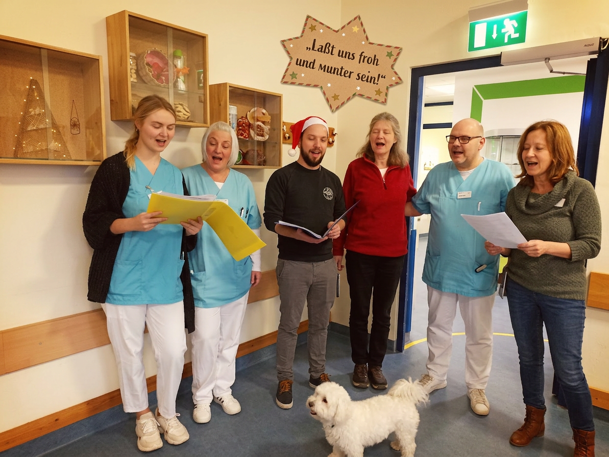 Group of six people singing indoors with a small white dog, some wearing medical scrubs and one with a Santa hat